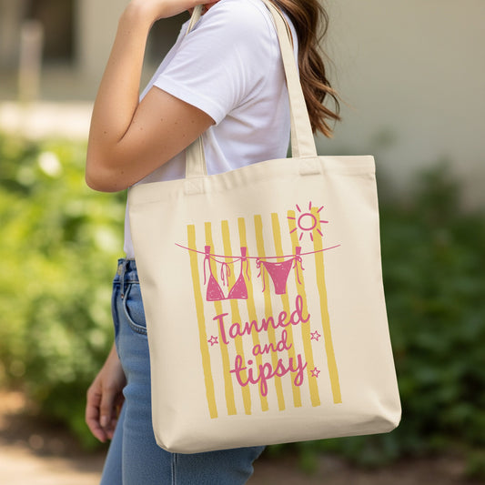 Canvas tote bag with "Tanned and tipsy" text and bikini and sun graphic.