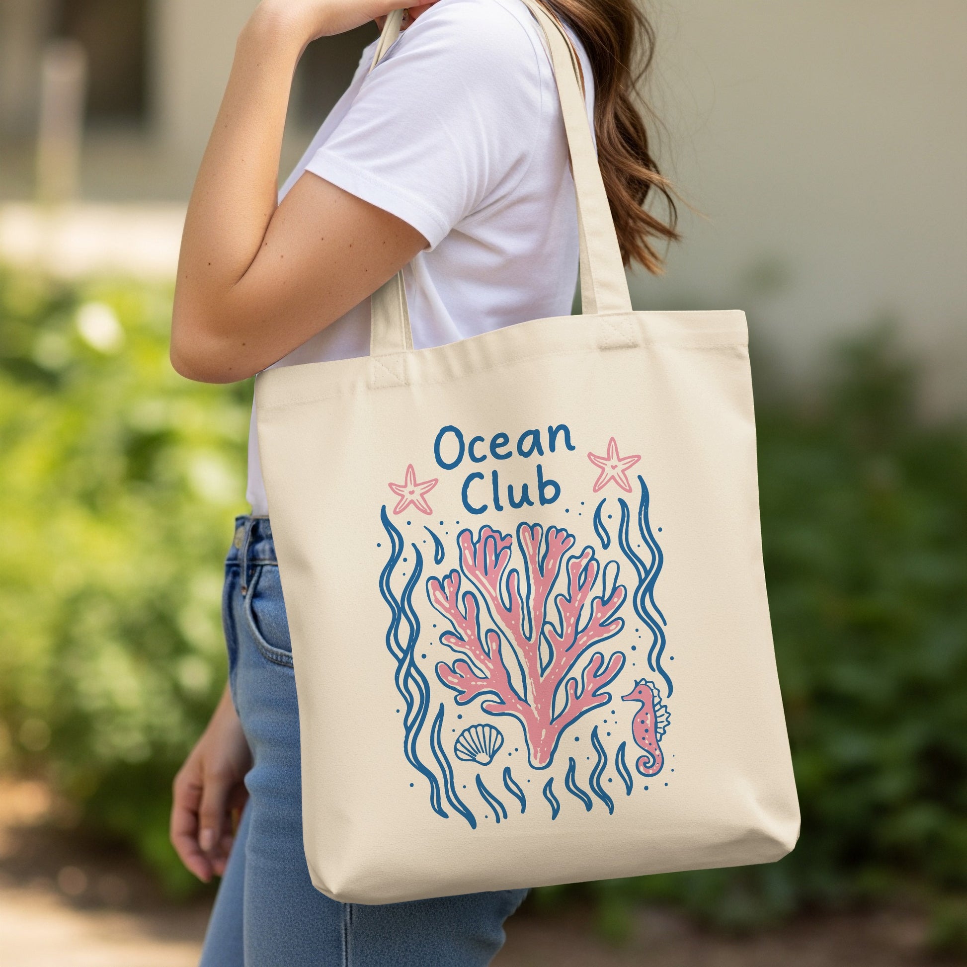 Beige tote bag with a pink coral, seahorse, and starfish illustration.